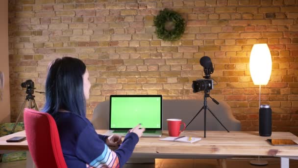 Närbild tillbaka syn på unga attraktiva kvinnliga bloggare Live streaming på den bärbara datorn med grön skärm inomhus i lägenheten — Stockvideo