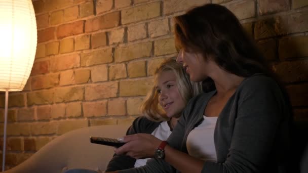 Primo piano della giovane madre caucasica e sua figlia che guardano la TV e usano il telecomando sorridente e seduta sul divano — Video Stock