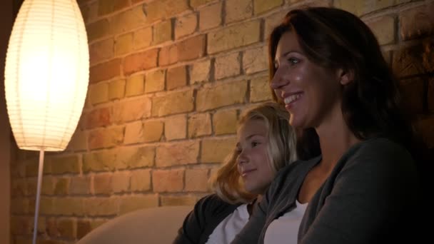 Closeup shoot of young caucasian mother and her daughter watching a cartoon on TV laughing and making comments — Stock Video