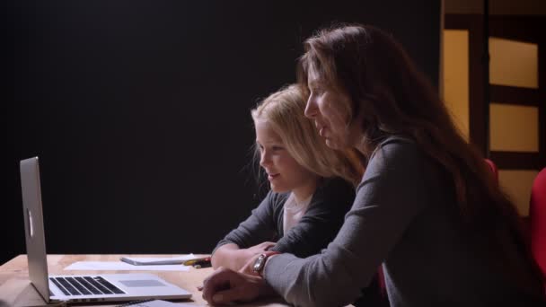 Крупним планом знімок молодої білої жінки і її солодкої маленької дочки дивитися фільм на ноутбуці і сміятися — стокове відео