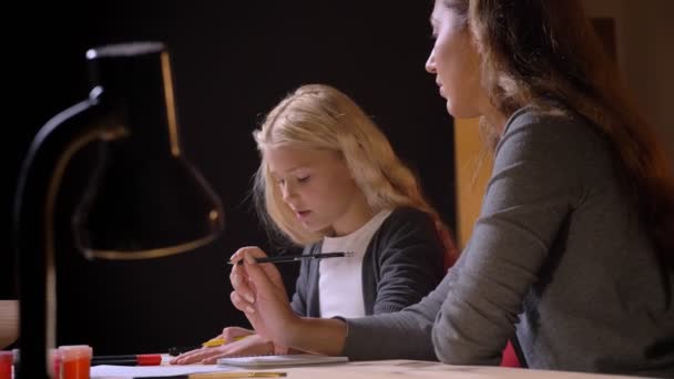 Portre çekimi genç beyaz anne küçük tatlı kızı izole siyah arka plan ile yardım — Stok video