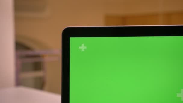 Съемка крупным планом с помощью камеры перемещается по офисному интерьеру и останавливается на зеленом хроматическом экране ноутбука — стоковое видео