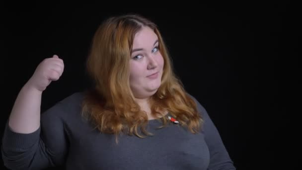 Nahaufnahme einer jungen übergewichtigen Kaukasierin, die einen Daumen nach oben zeigt, während sie fröhlich vor der Kamera lächelt — Stockvideo