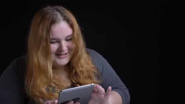 特写镜头拍摄年轻超重的高加索女性打字在平板电脑上和反应的社交媒体的帖子与背景隔离在黑色 — 图库视频影像