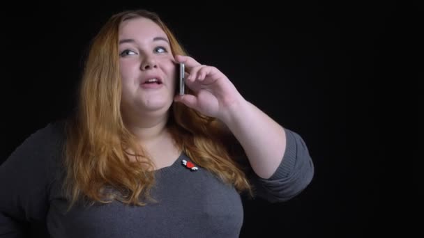 Closeup shoot of young overweight caucasian female having a casual conversation on the phone with background isolated on black. — Stock Video