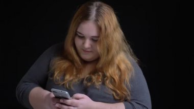 Genç kilolu neşeli beyaz kadın manifatura telefon ve şakacı izole siyah arka plan ile gülümseyen portre çekimleri