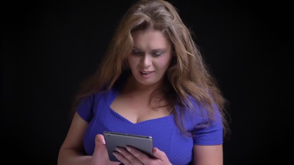 Retrato de primer plano de una mujer caucásica adulta usando la tableta y luego mirando a la cámara y sonriendo con el fondo aislado en negro — Vídeos de Stock