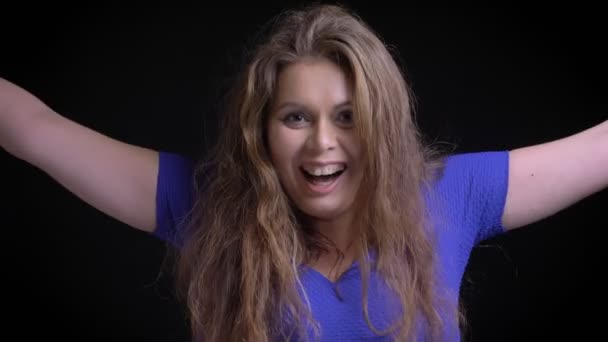 Nahaufnahme einer kaukasischen Frau mittleren Alters mit brünetten Haaren, die glücklich und aufgeregt lächelt und ihre Arme vor der Kamera in die Höhe reißt — Stockvideo