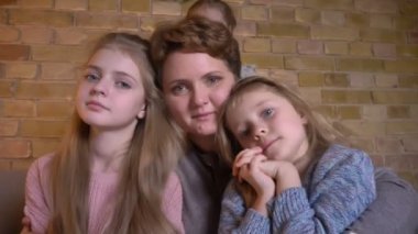 Beyaz anne ve üç kızı sarılma ve rahat ev atmosferde gülümseyerek kamera içine izlerken aile portresi.