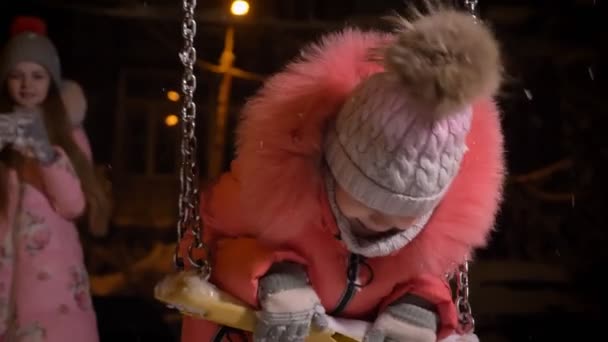 Yakın çekim küçük kız mutlu kış sokak arka plan üzerinde kamera içine izlerken salıncak üzerinde kırmızı paltolu portresi. — Stok video