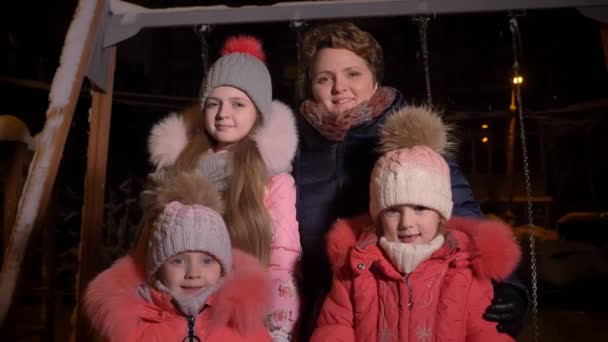 Сімейний портрет білої матері і трьох дочок, які їдять сніг і дивляться в камеру посміхаючись на вечірньому міському фоні . — стокове відео