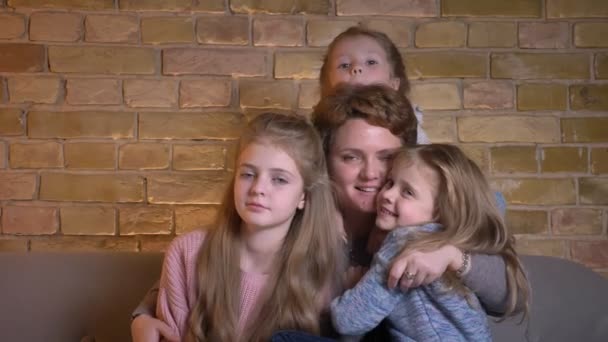 Retrato familiar de madre caucásica y tres hijas abrazándose y mirando a la cámara alegremente en un acogedor ambiente hogareño . — Vídeos de Stock