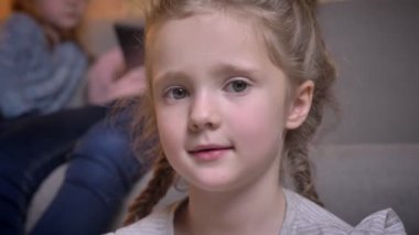 Utanarak kamera rahat ev ortamında içine gülümseyerek örgüler ile küçük oldukça beyaz kızın yakın çekim portre.