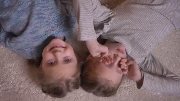 Portrait de deux petites filles drôles regardant volontiers dans la caméra couchée sur le sol . — Video