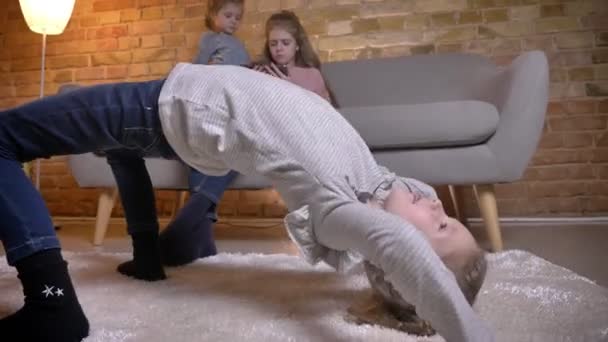 Retrato de una pequeña chica caucásica haciendo un puente con sus hermanas en el fondo . — Vídeos de Stock