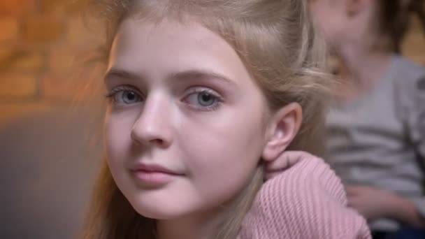 Närbild porträtt av små ganska kaukasiska flicka justera hennes hår och titta på lugnt in kameran i mysiga hem atmosfär. — Stockvideo