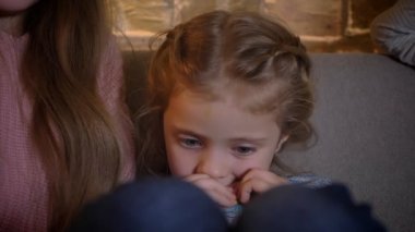 Küçük beyaz kız kanepede oturan ve rahat ev arka planda bir bisküvi yeme yakın çekim portresi.