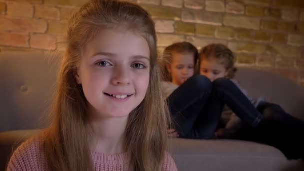 Close-up portret van vrij Kaukasische meisje glimlachend kijken en vreugdevol in camera met haar zusters op achtergrond. — Stockvideo