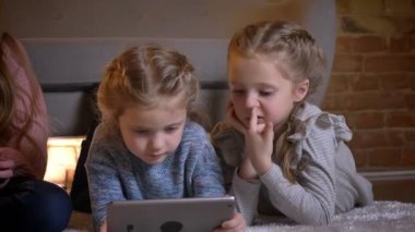 Yerde yatarken ve tablet rahat ev ortamında ilgi ile izlerken üç küçük beyaz kız portresi.