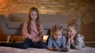 Katta oturan ve tablet ilgi ve rahat ev atmosferi ilgi ile izlerken üç küçük beyaz kız portresi