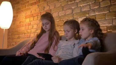 Üç küçük beyaz kızlar tablet ilgi ve rahat ev atmosferi ilgi ile izlerken portresi.