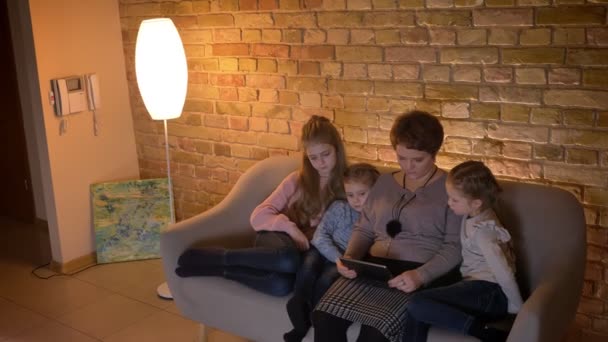 Top shot di madre caucasica e tre figlie guardando in tablet con attenzione e interesse per l'atmosfera accogliente casa . — Video Stock