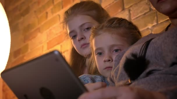 Gros plan portrait de deux mignonnes petites filles caucasiennes regardant attentivement dans la tablette dans une atmosphère confortable à la maison . — Video