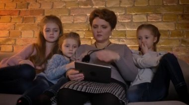 Beyaz anne ve kızları rahat ev atmosferde dikkatle tablet içine izlerken aile portresi.