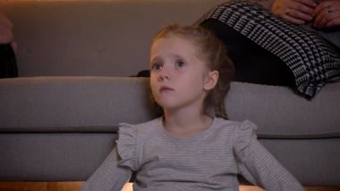 Küçük beyaz kızla yakın çekim portre rahat ev atmosferde dikkatle film seyrederken örgü.