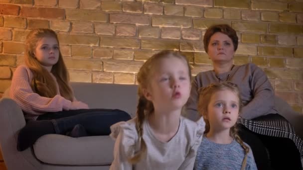 Portrait de famille de mère caucasienne avec trois filles assises ensemble et regardant le film attentivement dans une atmosphère confortable à la maison . — Video