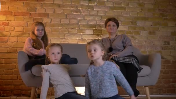 Retrato familiar de mãe caucasiana com três filhas abraçando uma à outra e assistindo filme em ambiente acolhedor casa . — Vídeo de Stock