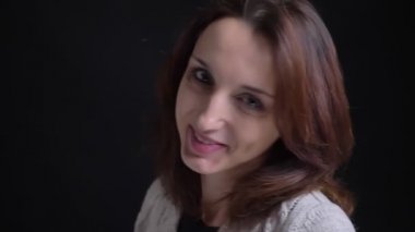 Kameraya dönüm, utanarak ve sevinçle siyah arka plan üzerine izliyorum orta yaşlı esmer beyaz bir kadın portresi.