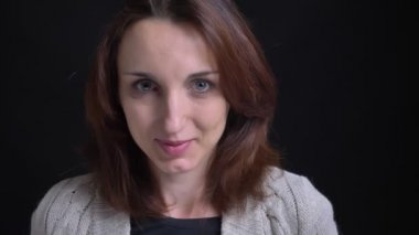 Utanarak içine kamera siyah arka plan üzerinde gülümseyen orta yaşlı esmer beyaz kadın portresi.
