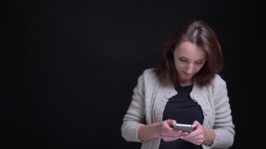 Smartphone ile çalışma ve siyah arka plan üzerine kamera içine izlerken orta yaşlı esmer beyaz bir kadın portresi.