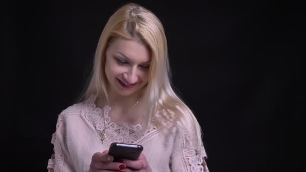 Close-up tiro de meia-idade mulher caucasiana usando o telefone e sorrindo com fundo isolado em preto — Vídeo de Stock