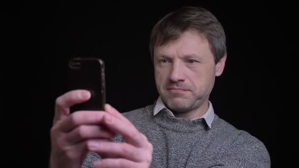 Zbliżenie strzelać dorosłych atrakcyjne kaukaski mężczyzna biorąc selfie na telefon z tła na czarnym tle — Wideo stockowe