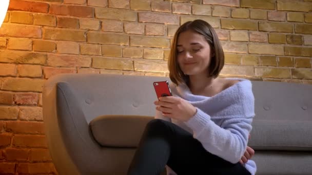 Gros plan pousse de jeune femme caucasienne mignonne en utilisant le téléphone et souriant assis sur le sol à la maison confortable à l'intérieur — Video