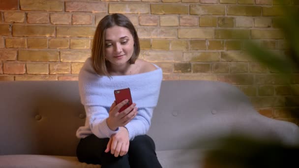 Vértes-lő a fiatal kaukázusi nő, miután egy video hív a phonesitting szobában kényelmes otthon a kanapén — Stock videók
