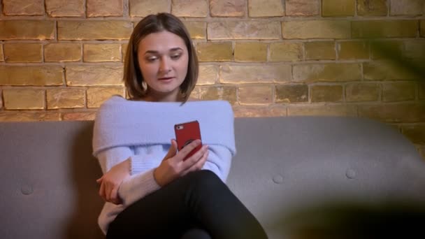 Zbliżenie strzelać z młody piękny kaukaski kobieta rozmowy za pośrednictwem rozmów wideo w telefonie siedzi na kanapie w przytulnym domu pomieszczeniu — Wideo stockowe