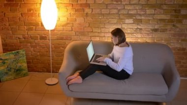 Closeup üst ateş genç beyaz kadın laptop kapalı rahat evde kanepede otururken yazmaktan