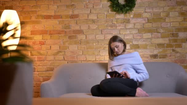 Closeup portrait of young beautiful caucasian female using the tablet and smiling while sitting on the sofa in cozy apartment indoors — Stock Video