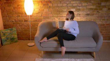 Closeup üst ateş dizüstü bilgisayarda yazarak ve ev kapalı kanepede oturan uzak iş genç beyaz kadın