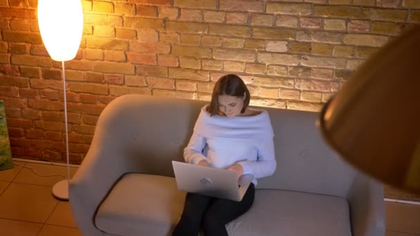 Closeup top shoot of young caucasian female typing on the laptop and studying online sitting on the couch indoors — Stock Video