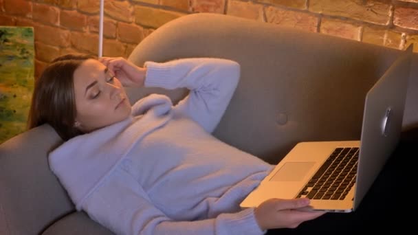 Closeup portrait of young caucasian female using the laptop lying on the sofa indoors — Stock Video