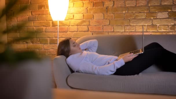 Zbliżenie strzelać z młodych kaukaski kobieta czytanie e-booków za pomocą tabletu leżąc na kanapie w przytulny dom wewnątrz — Wideo stockowe