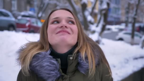 Tiro de close-up de jovem bela mulher caucasiana com cabelo morena sorrindo e sendo sonhadora na rua nevada em um dia de inverno — Vídeo de Stock