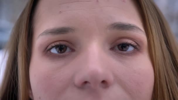 Retrato de close-up de jovem rosto feminino caucasiano atraente com belos olhos castanhos olhando diretamente para a câmera — Vídeo de Stock