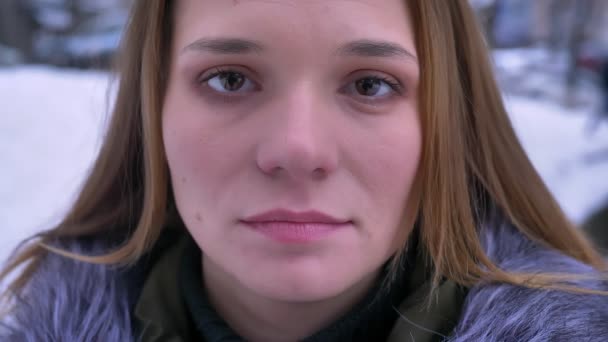 Closeup πυροβολούν από νεαρή όμορφη γυναίκα Καυκάσιος με μελαχρινή μαλλιά είναι ονειρική μπροστά από την κάμερα σε ένα χειμερινό παλτό σε μια χιονισμένη μέρα — Αρχείο Βίντεο