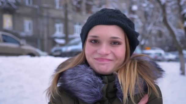 Primer plano de la joven atractiva hembra caucásica con la hembra morena sonriendo felizmente mientras mira a la cámara de pie al aire libre en un día de invierno nevado — Vídeo de stock