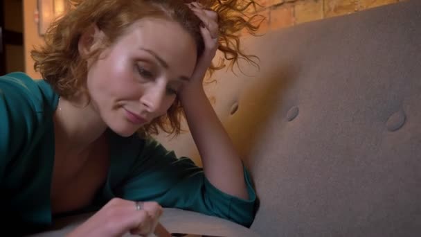 Szczegół portret profil zmęczony imbir kręcone włosy dziewczyna leżąc na kanapie i pisać na tablecie starannie na przytulnym domu tło. — Wideo stockowe